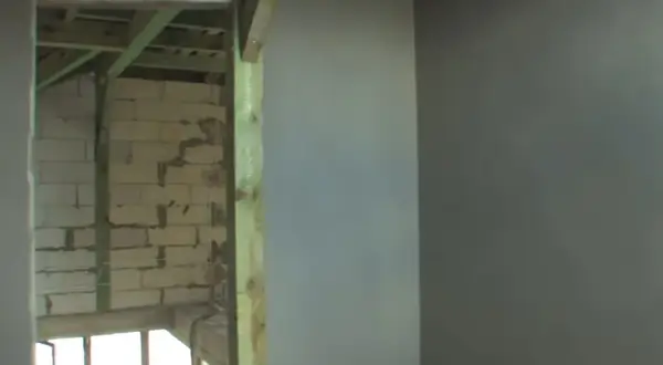 Ściana z tynkiem cementowo-wapiennym i widok na budowę w tle.